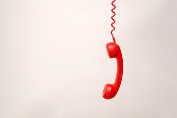 Red telephone receiver hanging by coiled cord on light grey background with copy space