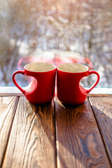 two heart shaped mugs with tea on the background of a window in winter
