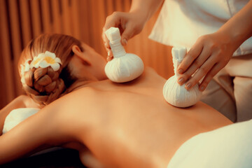 Hot herbal ball spa massage body treatment, masseur gently compresses herb bag on woman body....