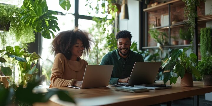 A warm and candid office moment of two colleagues seated at a wooden desk in a modern co-working space, smiling as they collaborate on a laptop