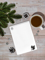 A cozy flat lay of a blank notebook paired with a cup of coffee, frosted pinecones, and festive snowflakes on a rustic wooden surface. Ideal for seasonal blogs, Christmas planning content, and cozy
