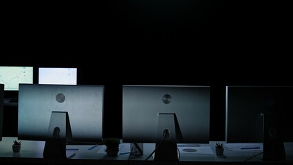 Men and women leaders team work at desks with monitors in dark office, yearend corporate meeting, empty room with few tables and desktop monitors and low light.