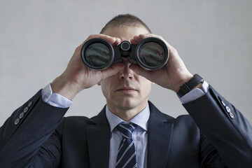 Man in a shirt and tie is spying on someone through binoculars.