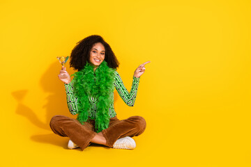 Young woman with curly hair and martini against a bright yellow backdrop in casual attire