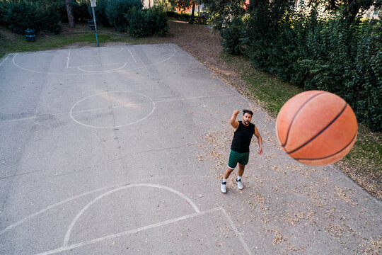 basketball player shoots the ball from a distance on a quiet outdoor court surrounded by greenery, emphasizing focus and skill under soft evening light with scattered leaves on the ground.