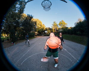 basketball player positions himself near the hoop with focus and determination on a tree-lined outdoor court under clear skies, highlighting athletic concentration and gameplay dynamics.