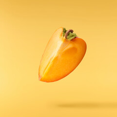 Fresh ripe Persimone fruit falling in the air isolated on yellow background, food levitation or zero gravity conception