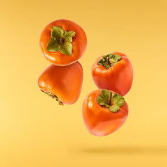 Fresh ripe Persimone fruit falling in the air isolated on yellow background, food levitation or zero gravity conception
