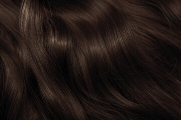 Brown hair close-up as a background. Women's long brown hair. Beautifully styled wavy shiny curls....