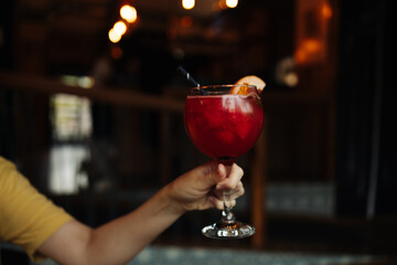 Woman hand holds glass of delicious chilled alcoholic strawberry drink with orange celebrating valentine's day in the bar. Bartender prepares a cocktail. High quality photo
