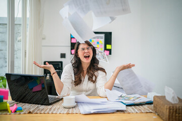 A stressed woman in a cluttered home office is throwing papers into chaos all around her