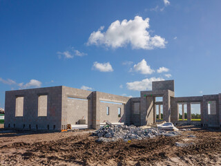 Concrete shell of a single-family house under construction, with a pile of discarded concrete blocks by bags of mortar mix, in a suburban residential development on a sunny morning in Florida