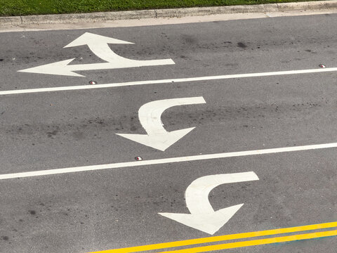 High-angle view of white directional arrows in three turn lanes near an intersection (off camera) of an urban one-way street downtown, for themes of alternatives, guidance, and impending decisions