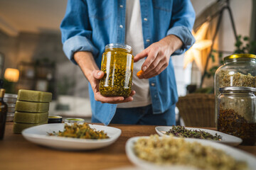 close up view of man herbalist hold oil with herbs in a jar