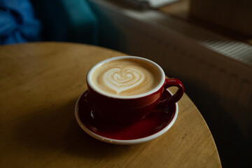 A red cup of latte art coffee on natural wood table. Close up with hot cappuccino with coffee art on the wooden table. High quality photo