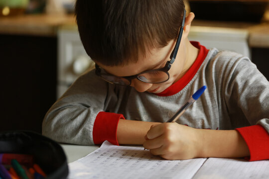 the boy is learning to write letters.The boy with glasses is doing his homework at home