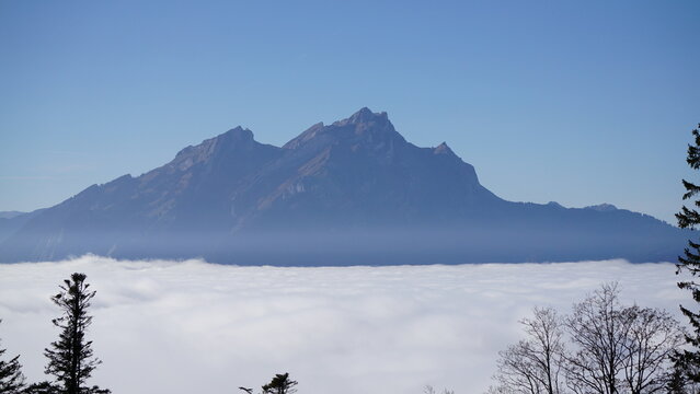 View of Pilatus mountain rising from low lying fog with clear blue sky in Switzerland