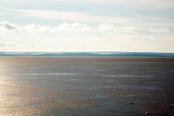 a snowy lake with a few trees and a sun shining on the water.