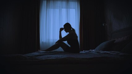 black silhouette upset unhappy woman sitting on bed dark room, mood depression sadness emotion. Sad lonely Girl feels bad after party, migraine suffers from headache. window curtains white fabric