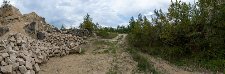 Limestone open-pit quarry. A pile of limestone rocks in front of the slope wall, road, and slope on the other side. Panorama. Mine in Jozefow, Poland, Europe.