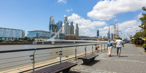 Panoramic view of a couple enjoying a walk on a sunny day in the neighborhood of Puerto Madero,...
