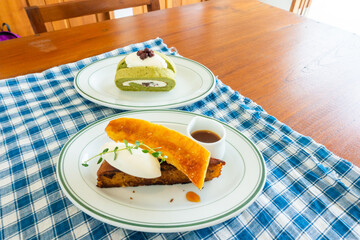 Matcha Green Tea Roll Cake and Salted caramel banana cake on blue classic checkered tablecloth texture,homemade bread cake,top view from above, space for text.