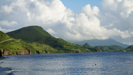 Blue, reflective ocean in foreground of lush, green mountains and white clouds