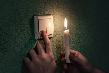 Holding burning candle in a dark room near a light switch, blackout. Power outage, energy crisis....