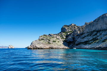 A bay of a rocky island in the Mediterranean with a pleasure motorboat in turquoise water on a sunny day.