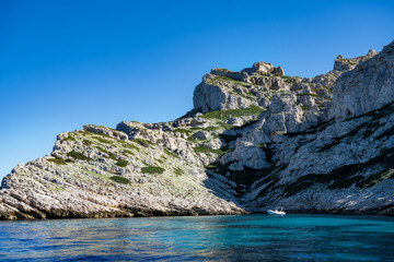 A bay of a rocky island in the Mediterranean with a pleasure motorboat in turquoise water on a sunny day.