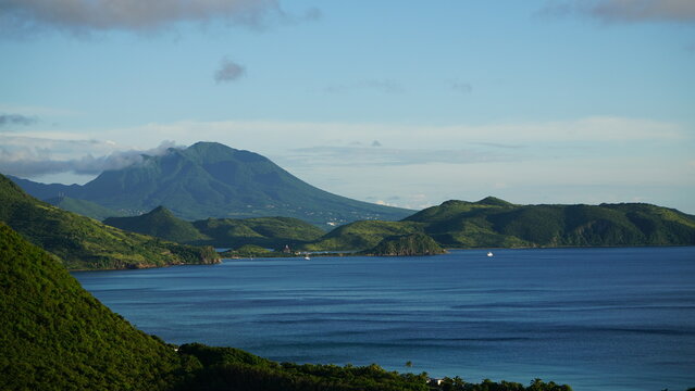 Landscape photo of the Caribbean Island of Saint Kitts & Nevis with view of turquoise blue water in a cove and lush green forest covered mountains.