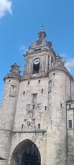 Fototapeta premium Detailreiche Ansicht eines imposanten historischen Steinturms mit prächtiger Uhr und skulpturalem Schmuckwerk unter klarem, blauem Himmel.
