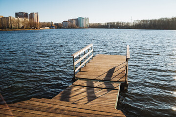 Fototapeta premium A beautifully designed wooden dock reaches out into the serene and calm waters of the lake, creating a striking contrast with the lively, vibrant cityscape that lies in the background