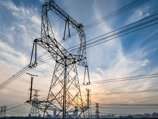 High voltage electricity towers and city skyline with cloudscape at sunset