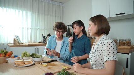 Happy father move to music while cooking food and prepare lunch at modern kitchen. Active dad dancing to song while making healthy food or salad surrounded with vegetable and kitchenware. Pedagogy.