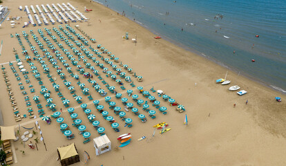 Aerial view of a lido on a large and crowded sandy beach. There are many people on vacation under...