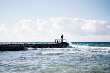 a portrait of a young man on a pier, waves splashing and crashing against the pier