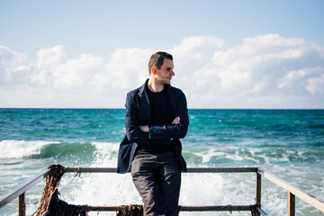 a portrait of a young man on a pier, waves splashing and crashing against the pier