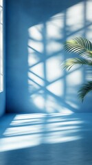 Obraz premium Sunlight casts geometric shadows through a window onto a blue wall, creating a serene interplay of light and shadow. A lone palm frond adds a touch of nature.