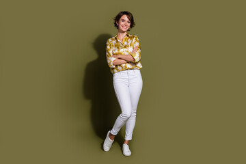Confident young woman with brunette hair wearing elegant blouse stands against khaki background,...