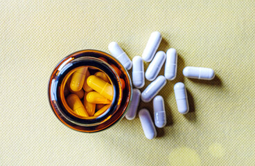 Top view of pills capsules in pill bottle on yellow background. White pills capsules medicine or ...