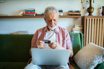 Senior man online shopping with laptop on couch at home