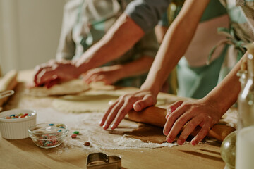 Hands carefully rolling dough and adding colorful sprinkles while baking cookies on kitchen counter. Small bowls of ingredients and cutters visible, creating a cozy baking scene