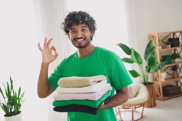 Portrait of nice young man hold towels show okey symbol wear t-shirt modern green interior flat indoors