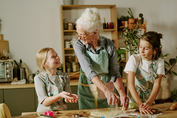 Elderly woman baking with two children in cozy kitchen, engaging in fun and educational activity....