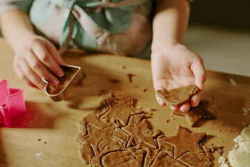 Hands cutting gingerbread dough on table, using star-shaped cookie cutters, creating festive...
