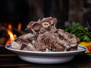 Against the background of a fireplace with burning logs, there is a plate of boiled meat, from which steam rises.