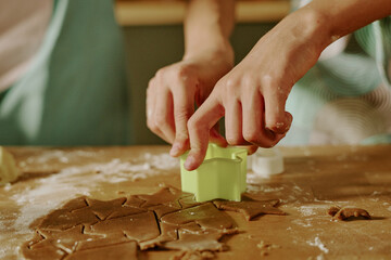 Hands using cookie cutter for crafting shapes from gingerbread dough in cozy kitchen environment during family gathering