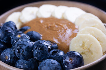 Close up on breakfast with whole oat, oat milk, chia seeds, banana, fresh blueberries, natural peanut butter and honey on white background