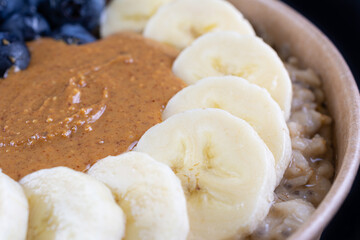 Perfect breakfast with whole oat, oat milk, chia seeds, banana, fresh blueberries, natural peanut butter and honey on black background